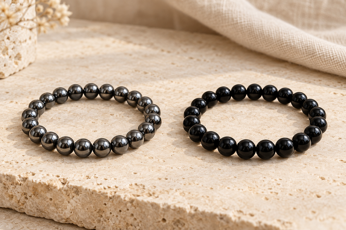  Metallic gray hematite bracelet beside a polished black obsidian bracelet on a beige stone surface.