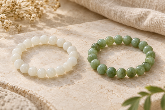 White jade and green jade bead bracelets displayed side by side on a beige stone surface.
