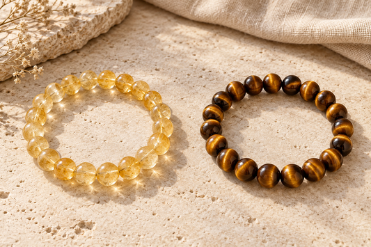 Golden yellow citrine and golden-brown tiger’s eye bead bracelets displayed side by side on a beige stone surface.