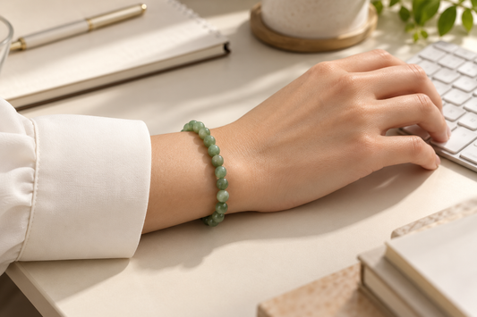 Green gemstone bead bracelet worn with a white shirt beside a keyboard on an office desk.