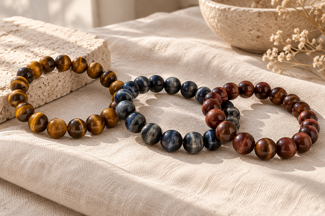 Golden-brown, blue-gray, and red-brown tiger’s eye-style bracelets arranged on ivory linen